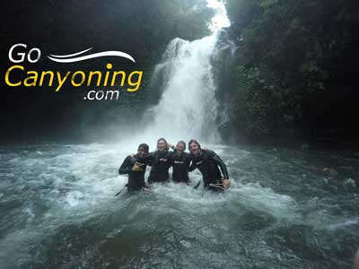 Four people standing in white water at the base of a waterfall gocanyoning.com